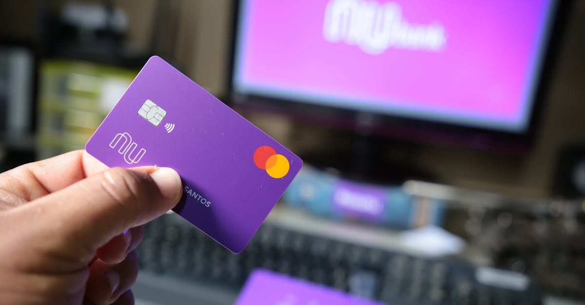 A close-up of a hand holding a purple bank card in front of a computer screen.